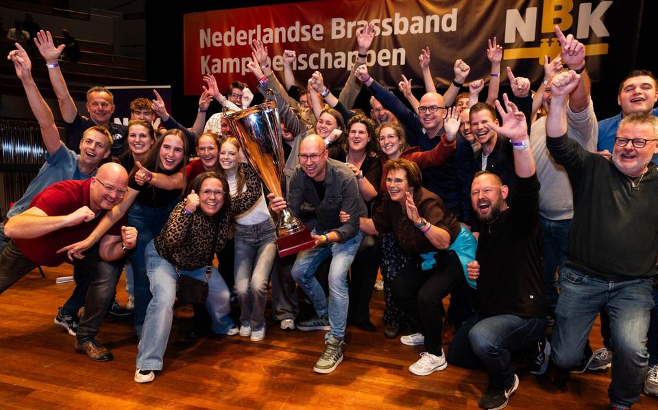 Brassband De Bazuin Oenkerk viert de nationale titel. Dirigent Jaap Musschenga tilt de kampioensbeker, uiterst rechts juicht es-kornettist Auke Douwes. 