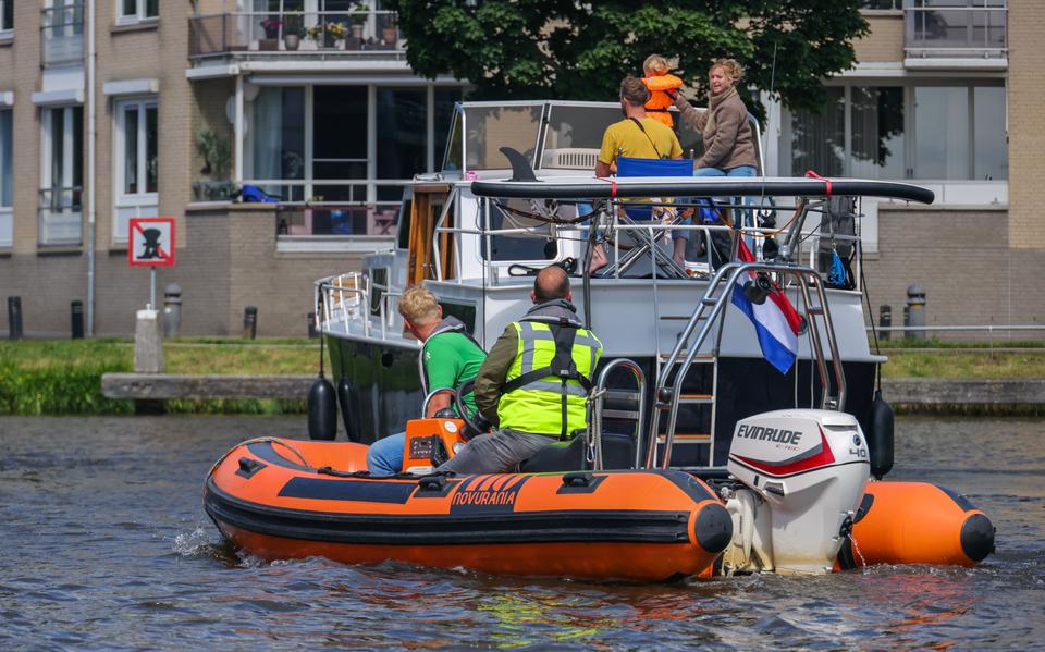 Op het Somerrak in Sneek varen waterstewards Pim de Reus (groen shirt) en Maarten naar een kruiser om uit te leggen dat ze aan moeten sluiten in de wachtrij voor de brug. 