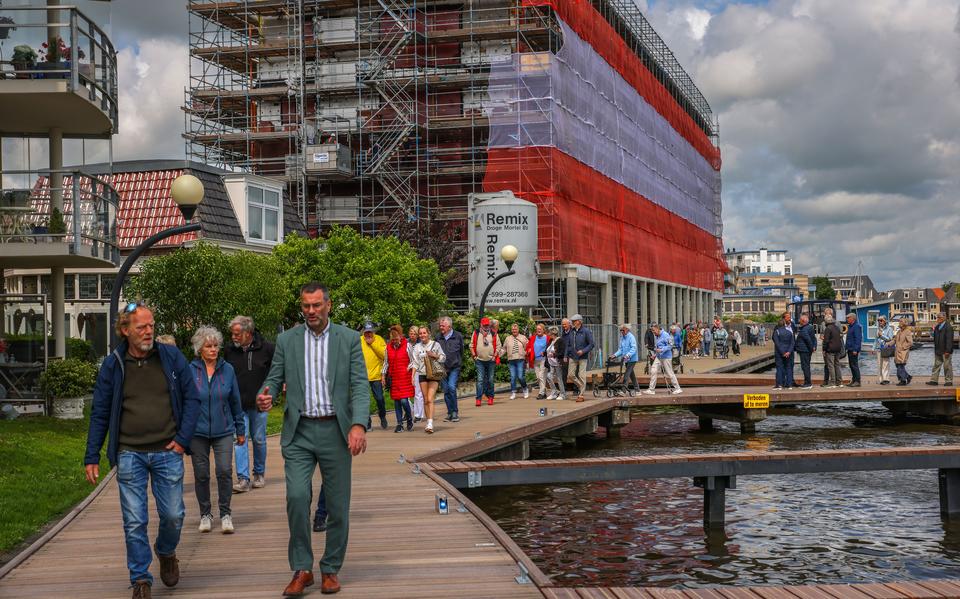 Genodigden lopen over de net heropende Somerrakpromenade in Sneek met op de achtergrond de nieuwbouw op het Flexaterrein. Rechts vooraan wethouder Henk de Boer van Súdwest-Fryslân.