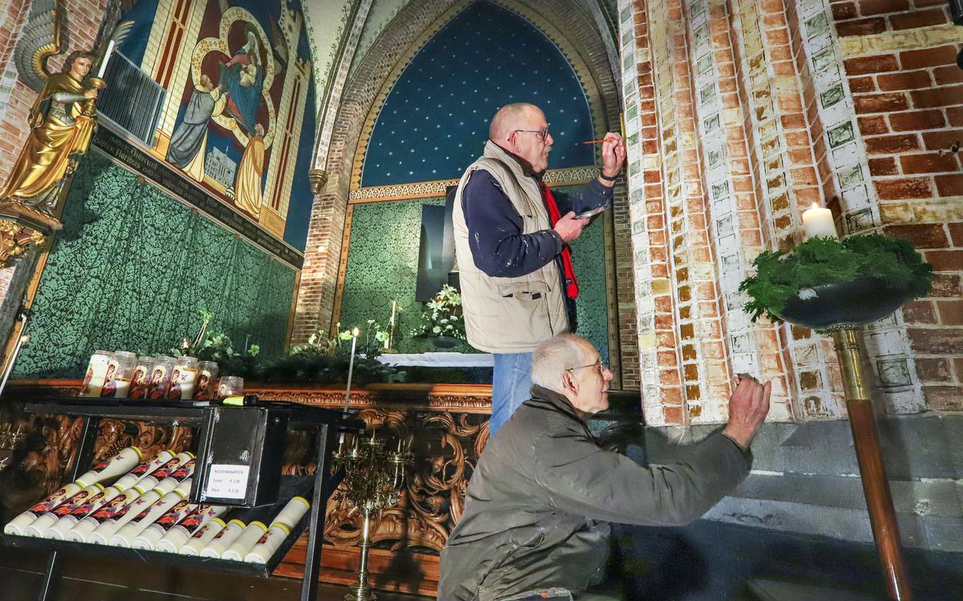 Olav van Overbeek (onder) en André Bekema werken beschadigde schilderingen bij in de Sneker Sint Martinuskerk.  