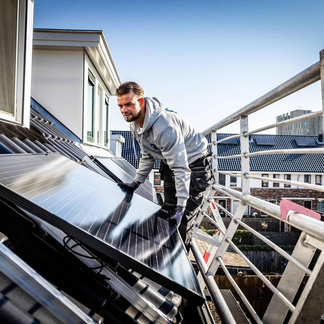 Een monteur legt zonnepanelen op een dak.