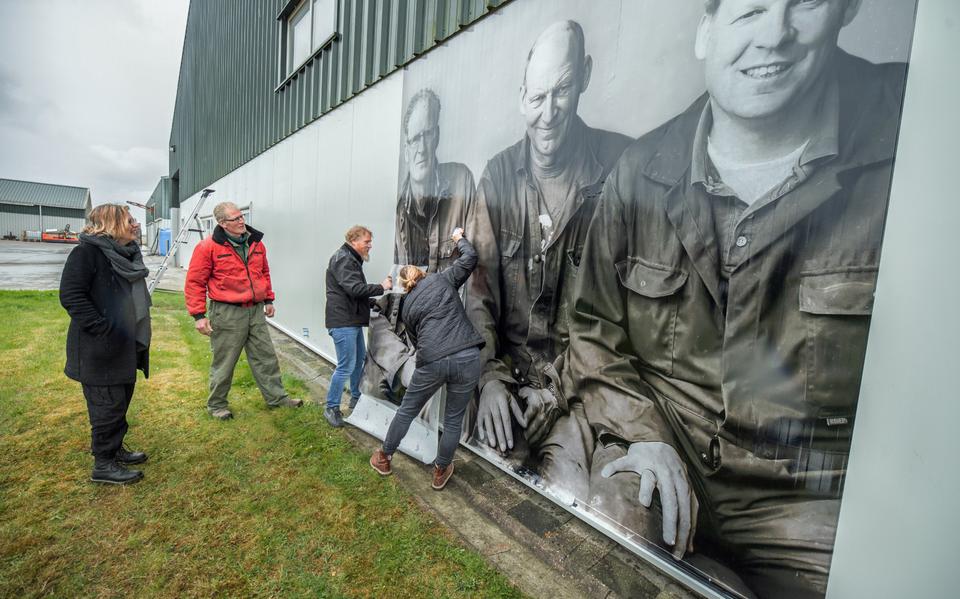 Wendy Gooren en Gerlof Jensma kijken toe hoe een metershoog portret van Gerlof, broer Sjoerd en de drie zonen van broer Goffe op een van de schuren wordt aangebracht.