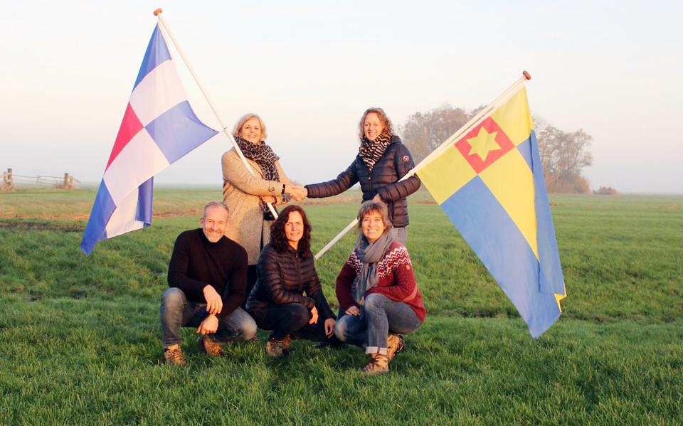 De initiatiefnemers van een bijzondere kuier door Noardeast-Fryslân wisselen halverwege de tocht tussen Westergeast en Dokkum de dorpsvlaggen uit, met links Lianne de Lange met de vlag van Munnekezijl en rechts Hanneke Jouta met de Ferwerter vlag. Op de foto verder v.l.n.r: Jan Roelof Buruma, Froukje Grijpstra en Mieke Yedema.