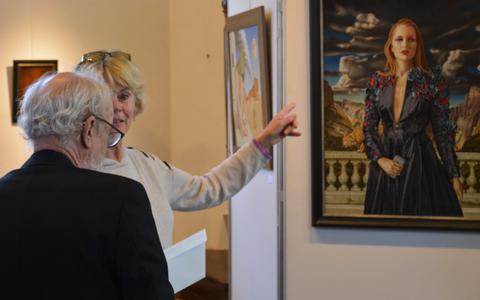 Kunstschilder Hans Berghuis (links) in gesprek met een bezoekster van Galerie Mildam. Rechts is zijn werk te zien.