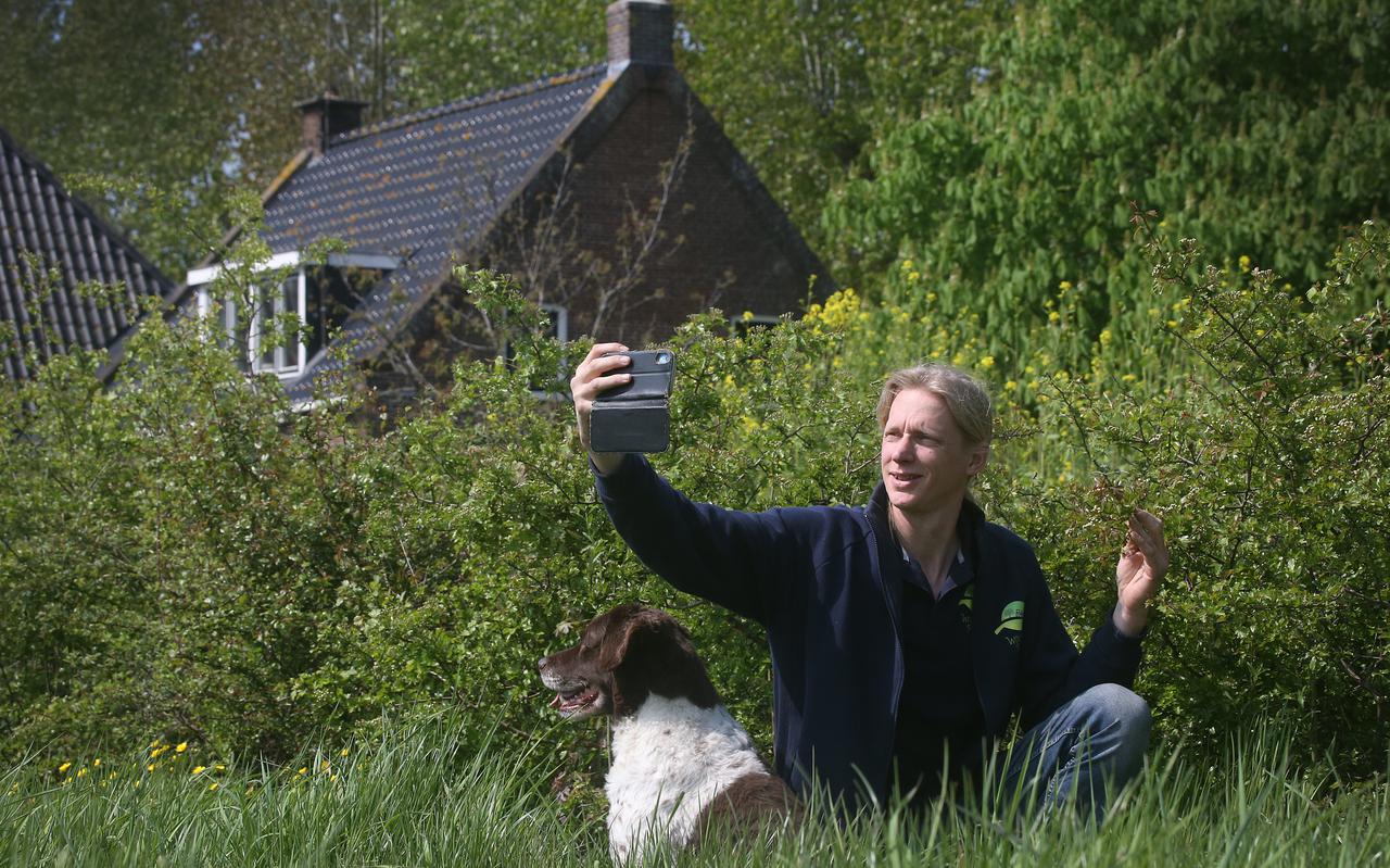 Jan Woudstra met iPhone en hond bij de voederhagen op zijn erf. Omdat hij het idee achter de hagen wilde promoten, begon hij met het maken van video's op TikTok.