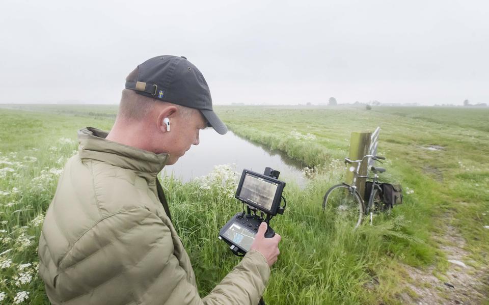 Langs de rand van het weiland kijkt Simon Spriensma naar de beelden van de drone, die verderop boven de landerijen vliegt. De fiets van boer Hans staat tegen de paal op de 'hikkedaam'. 