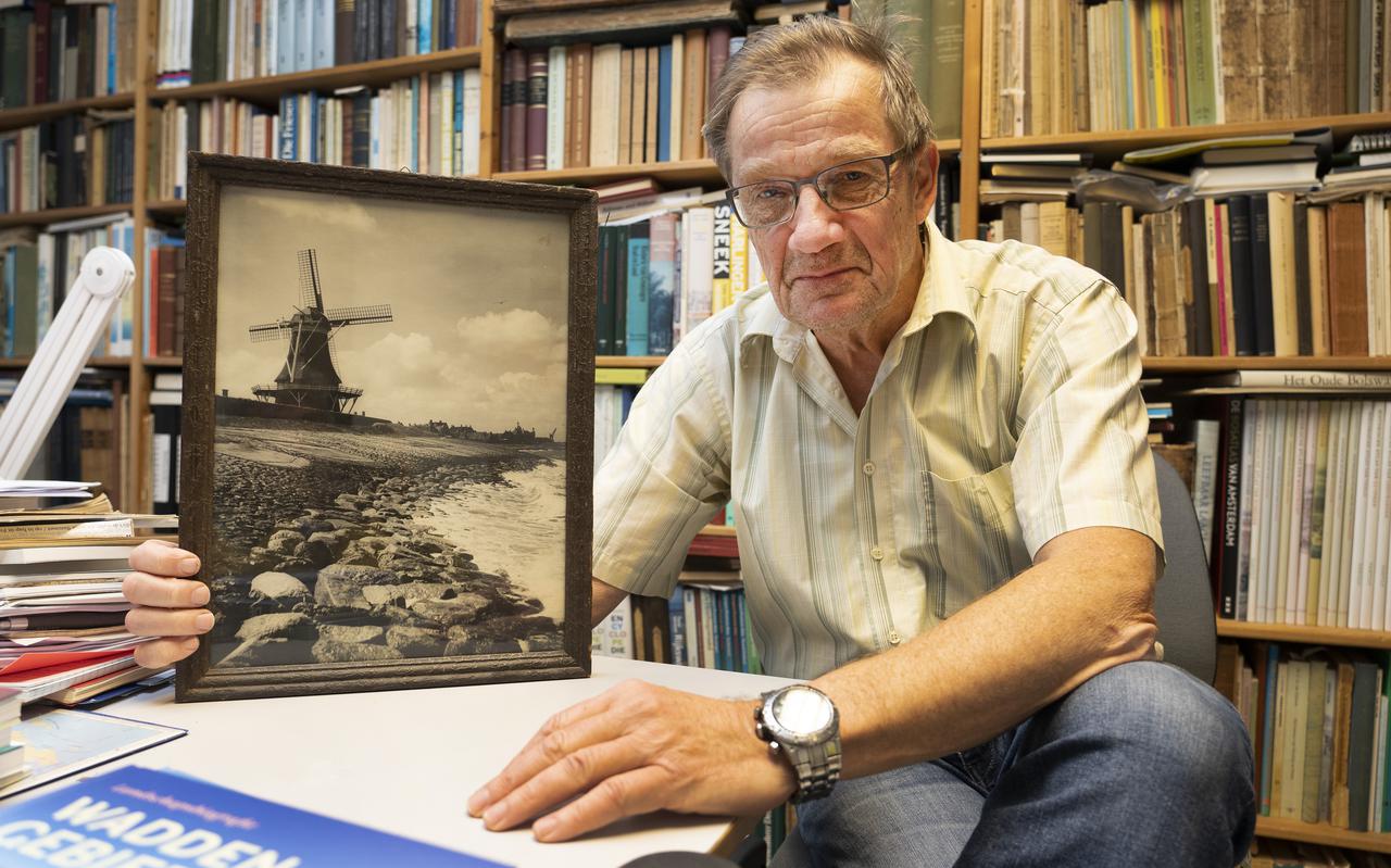 Meindert Schroor toont in zijn werkkamer een foto van een molen op de Waddendijk bij Harlingen. Nu maakt hij zich zorgen over de mogelijke komst van grote windmolens op de dijken. 