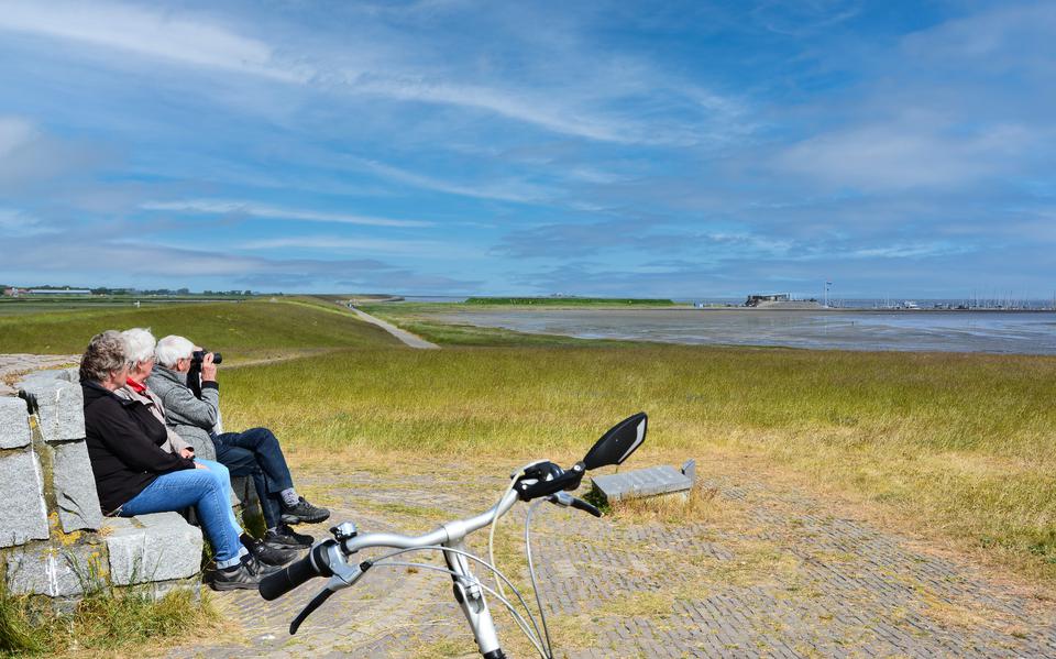 Drie toeristen rusten uit op het bankje van John Eric Bank, tussen de Waddenzee en de Westerplas. Dit bankje markeert het begin van de zeedijk van Schiermonnikoog en loopt vanaf daar vier kilometer oostwaarts. 