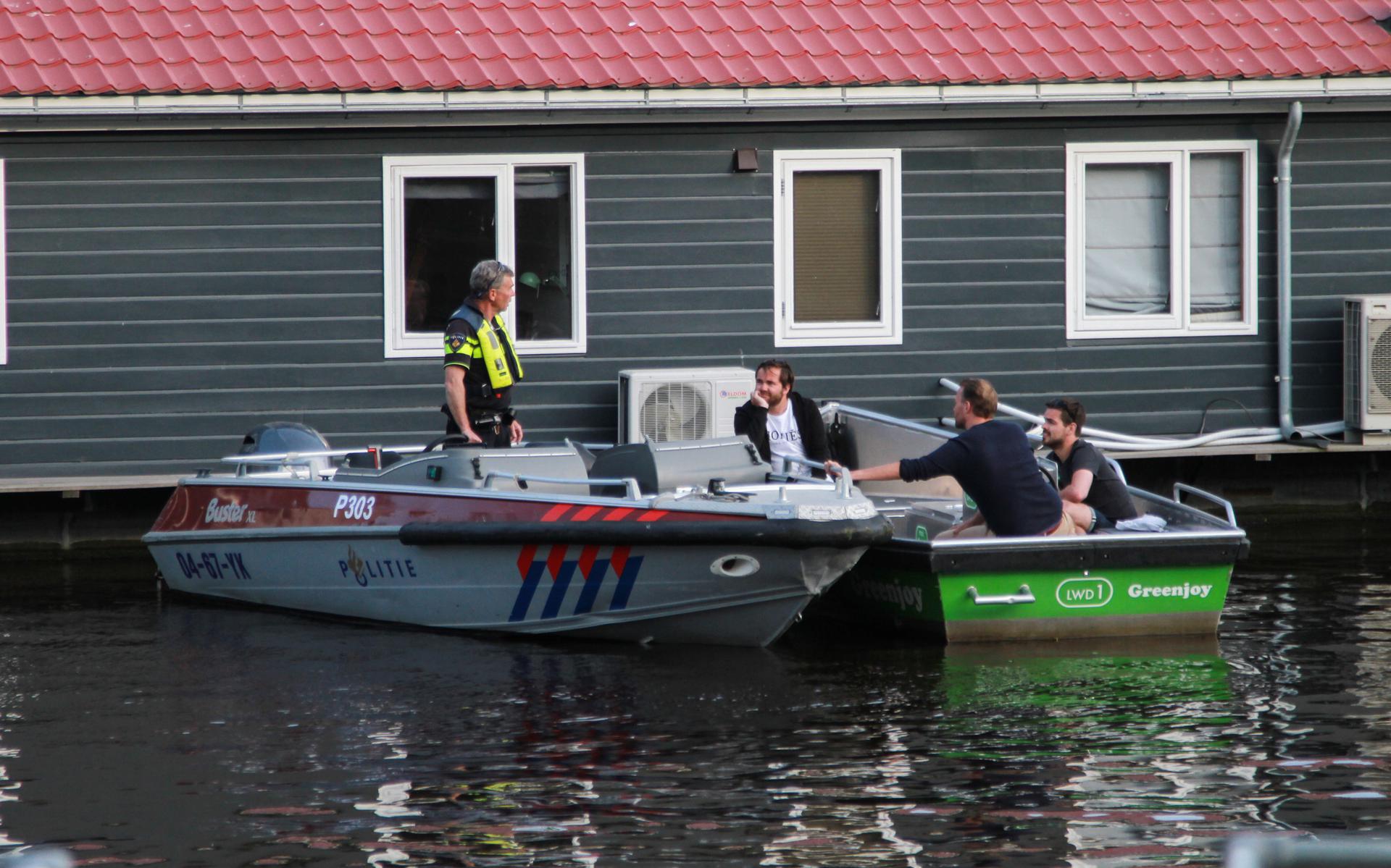 Een politieagent in Leeuwarden in gesprek met drie mannen op een bootje over de afstandsregel.