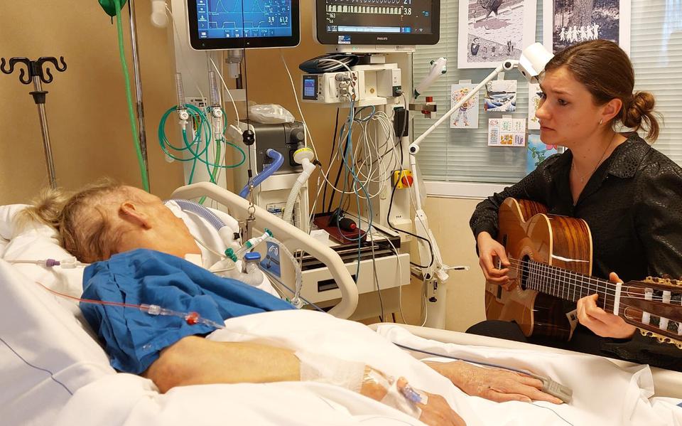 Muziektherapeut Eline van der Veen speelt gitaar voor een patiënt op de IC van Nij Smellinghe. 