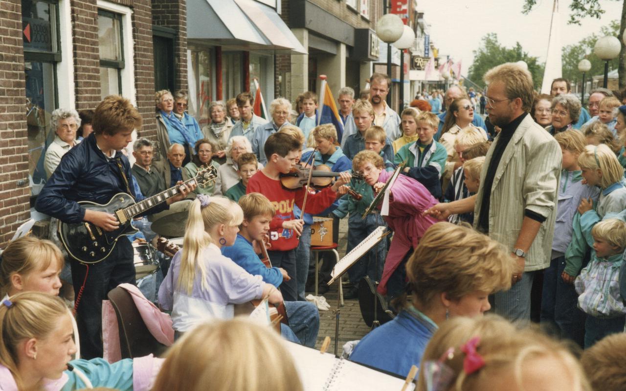 Optreden van het schoolorkest van Terwispeler basisschool It Ambyld in het centrum van Gorredijk. Meester Libbe de Vries (rechts) dirigeert. Staand links, met elektrische gitaar: Arvan Blok.