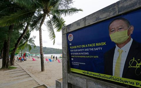 Een overheidsposter die toeristen op het strand van Phuket (Thailand) wijst op de mondkapjesplicht. 